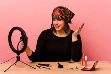 Makyaj sanatçısı genç bir kadın pembe arka planda özel bir makyaj dersi veriyor.