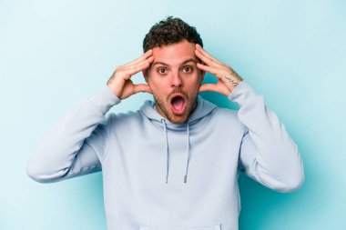 Mavi arka planda izole edilmiş genç beyaz adam hoş bir sürpriz alıyor, heyecanlı ve el kaldırıyor..