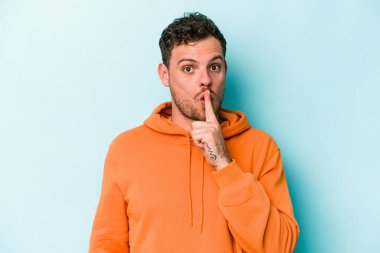 Mavi arka planda izole edilmiş genç beyaz bir adam ya sır saklıyor ya da sessizlik istiyor..