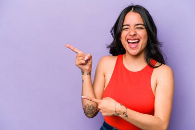 Mor arka planda izole edilmiş genç İspanyol kadın işaret parmaklarıyla fotokopi alanını işaret ederek heyecan ve arzusunu ifade ediyor..