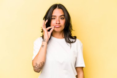 Sarı arka planda izole edilmiş genç İspanyol kadın parmakları dudaklarında bir sır saklıyor..