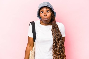 Genç Afrikalı Amerikalı bir kadın pembe arka planda izole bir şekilde sahile gidiyor omuzlarını silkiyor ve gözleri açık..