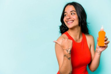 Mavi arka planda güneş kremi tutan genç İspanyol kadın parmak uzakta, gülüyor ve kaygısız..