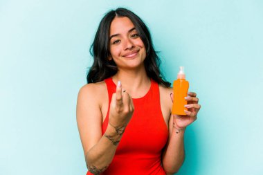 Mavi arka planda güneş kremi tutan genç İspanyol kadın sanki seni davet ediyormuş gibi seni işaret ediyor..