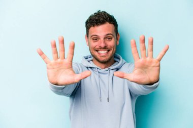Mavi arka planda izole edilmiş genç beyaz adam on numarayı elleriyle gösteriyor..
