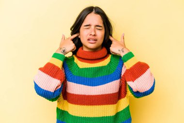 Sarı arka planda izole edilmiş, parmaklarıyla kulaklarını kapatan genç İspanyol kadın, gürültülü bir ortam yüzünden stresli ve çaresiz..