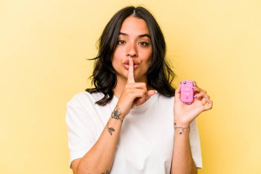 Pembe arka planda izole edilmiş anahtar taşıyan genç İspanyol kadın ya sır saklıyor ya da sessizlik istiyor..