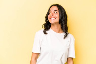 Sarı arka planda izole edilmiş genç İspanyol kadın rahatlamış ve mutlu bir şekilde gülüyor, boynunda dişlerini gösteriyor..