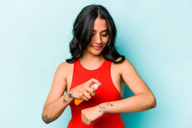 Mavi arka planda güneş kremi tutan genç İspanyol kadın.