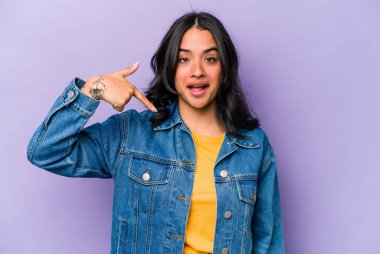 Mor arka planda izole edilmiş genç İspanyol kadın gömlek fotokopisini elle gösteriyor, gururlu ve kendinden emin.