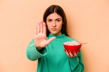 Latin kökenli genç bir kadın bej arka planda izole edilmiş mısır gevreği yiyor..