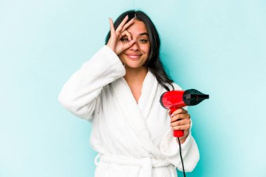 Mavi arka planda izole edilmiş kurutma makinesini tutan genç İspanyol kadın heyecanlı..