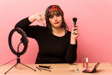 Makyaj sanatçısı genç bir kadın pembe arka planda izole edilmiş makyaj dersi veriyor. Hoşlanmadığı bir jest gösteriyor. Anlaşmazlık konsepti.