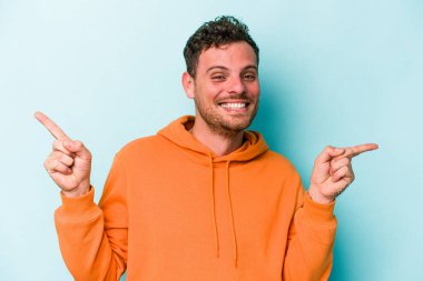 Mavi arka planda izole edilmiş genç beyaz adam farklı kopya alanlarını gösteriyor, birini seçiyor, parmaklarıyla gösteriyor.