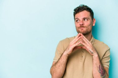 Kafkasyalı genç bir adam mavi arka planda izole edildi. Aklında bir plan kuruyor, bir fikir kuruyor..