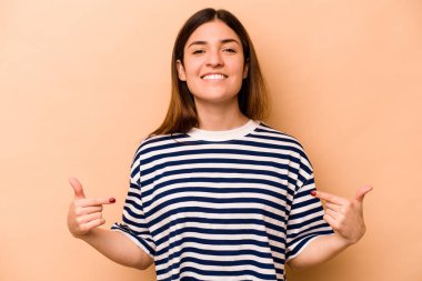 Latin kökenli genç bir kadın bej arka planda izole edilmiş. Parmakları aşağıda, olumlu hisler içinde..