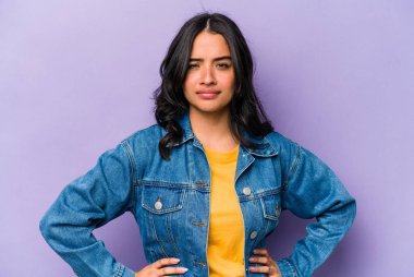 Mor arka planda izole edilmiş, hoşnutsuzca kaşlarını çatmış, kollarını kavuşturmuş genç bir İspanyol kadın..