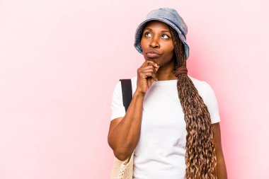 Genç Afrikalı Amerikalı bir kadın pembe arka planda izole edilmiş bir şekilde sahile gidiyor. Şüpheli ve şüpheci bir ifadeyle yana bakıyor..