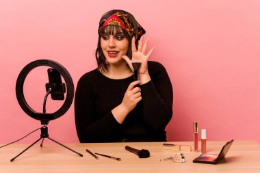 Makyaj sanatçısı genç bir kadın pembe arka planda özel bir makyaj dersi veriyor.