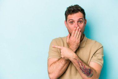 Mavi arka planda izole edilmiş genç beyaz adam yan tarafı işaret ediyor.