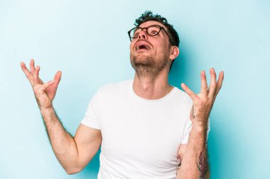 Kafkasyalı genç adam mavi arka planda izole edilmiş gökyüzüne haykırıyor, yukarı bakıyor, hayal kırıklığına uğramış..