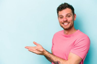 Mavi arka planda izole edilmiş genç beyaz bir adam palmiyesinde bir kopya alanı tutuyor..