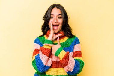 Latin kökenli genç bir kadın sarı arka planda izole edilmiş. Dedikodu yapıyor, bir şeyleri bildiriyor..