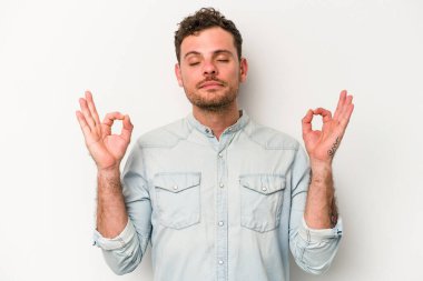 Beyaz arka planda izole edilmiş genç beyaz adam yoğun bir günün ardından rahatlıyor. Yoga yapıyor..