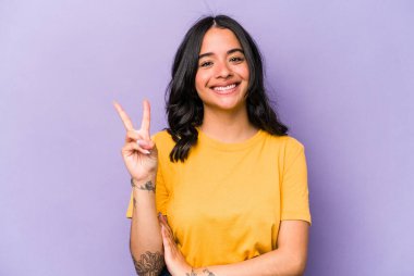 Mor arka planda izole edilmiş genç İspanyol kadın iki numarayı parmaklarıyla gösteriyor..