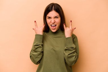 Latin kökenli genç bir kadın bej arka planda izole edilmiş boynuzlarını devrim konsepti olarak gösteriyor..