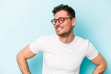 Kafkasyalı genç, mavi arka planda izole edilmiş. Kendine güvenen, kalçaları tutan biri..