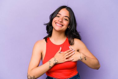 Mor arka planda izole edilmiş genç İspanyol kadın, avuçlarını göğsüne bastıran dostça bir ifadeye sahiptir. Aşk konsepti.