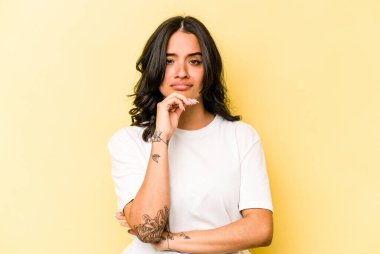 Genç İspanyol kadın sarı arka planda izole edilmiş düşünüyor, bakıyor, yansıtıyor, düşünüyor, hayal kuruyor..