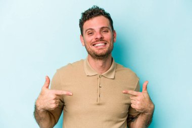 Kafkasyalı genç adam mavi arka planda izole edildi. Parmakları aşağıda, olumlu bir his var..