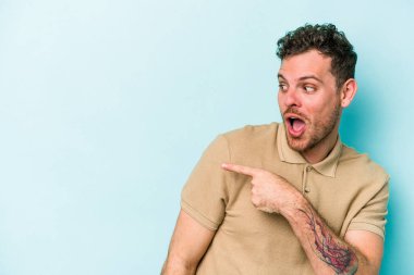 Kafkasyalı genç adam mavi arka plan noktalarında izole edilmiş başparmak uzakta, gülüyor ve kaygısız.