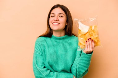 Genç İspanyol kadın elinde bir paket cipsle bej arka planda gülüyor ve eğleniyor..