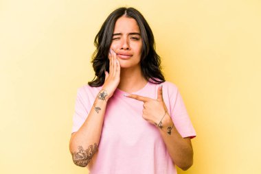 Sarı arka planda izole edilmiş genç İspanyol kadın güçlü bir diş ağrısı, azıdişi ağrısı var..