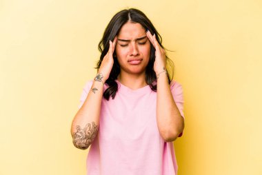 Sarı arka planda izole edilmiş genç İspanyol kadın şakaklara dokunuyor ve baş ağrısı çekiyor..