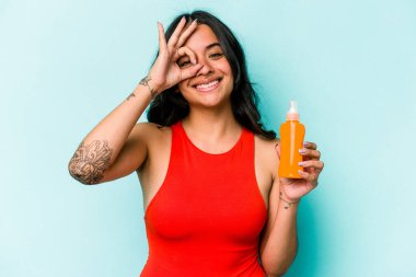 Mavi arka planda güneş kremi tutan genç İspanyol kadın heyecanlı..