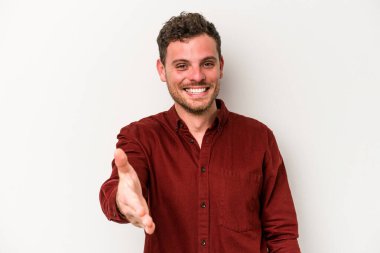 Beyaz arka planda izole edilmiş genç beyaz bir adam selamlama jesti olarak kameraya elini uzatıyor..