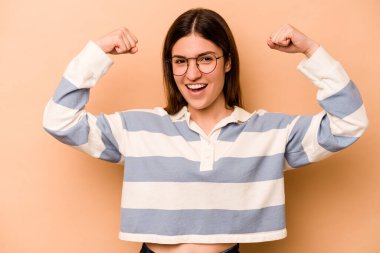 Latin kökenli genç bir kadın, bej arka planda izole edilmiş. Güçlü hareketler sergiliyor. Kadınsı gücün sembolü.