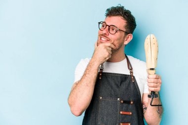 Kafkasyalı genç kunduracı mavi arka planda izole edilmiş şüpheli ve şüpheci bir ifadeyle yana bakıyor..