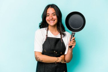 Young hispanic cooker woman holding frying pan isolated on blue background laughing and having fun.
