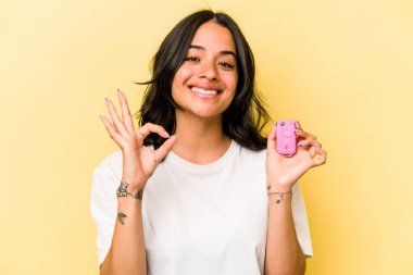 Pembe arka planda izole edilmiş anahtar taşıyan Latin kökenli genç bir kadın neşeli ve kendinden emin bir hareket sergiliyor..