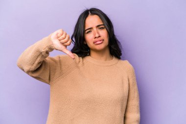 Mor arka planda izole edilmiş genç İspanyol kadın baş parmağını aşağı gösteriyor ve hoşlanmadığını ifade ediyor..