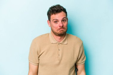 Mavi arka planda izole edilmiş genç beyaz adam omuzlarını silkeliyor ve gözleri açık..