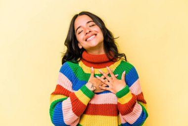 Sarı arka planda izole edilmiş genç İspanyol kadın, dost canlısı bir ifadeye sahip, avuçlarını göğsüne bastırıyor. Aşk konsepti.