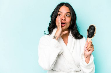 Mavi arka planda saç fırçası tutan genç İspanyol kadın gizli bir sıcak fren haberi veriyor ve yana bakıyor.