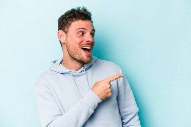 Mavi arka planda soyutlanmış genç beyaz bir adam gülümsüyor, neşeli ve keyifli görünüyor..