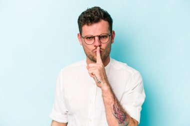 Mavi arka planda izole edilmiş genç beyaz bir adam ya sır saklıyor ya da sessizlik istiyor..